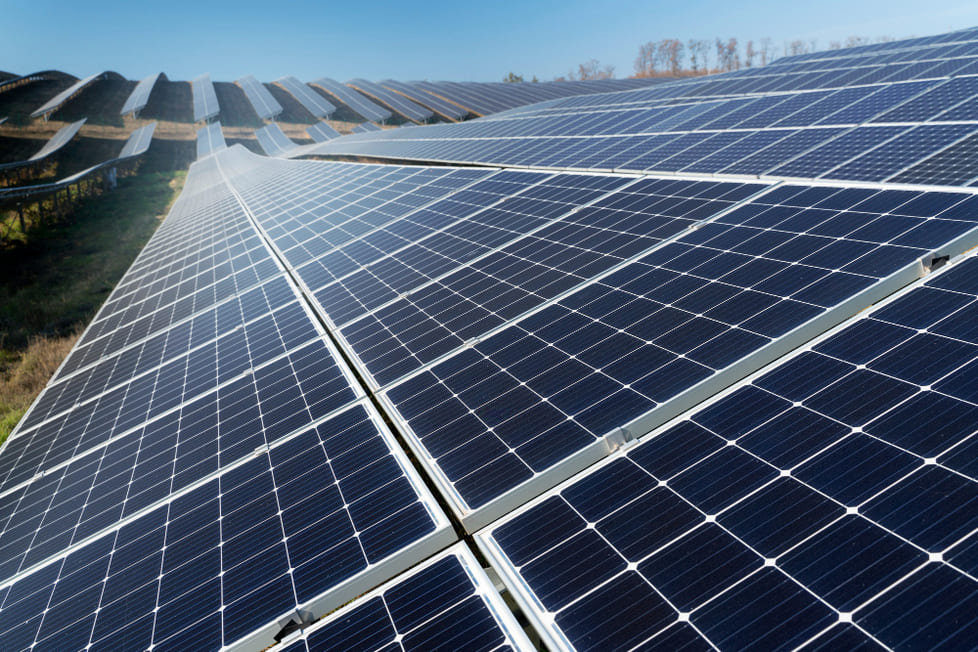 imagem contendo paineis solares em um campo verde com um céu azul de fundo.